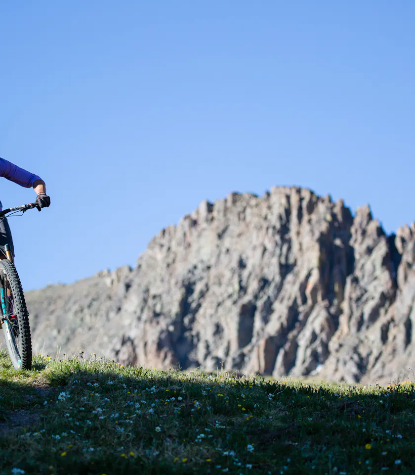 NIchole Baker riding high above treeline with jagged mountains in the background. 